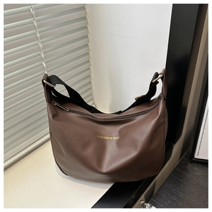 Détail d'un sac demi-lune en cuir mat marron avec lettrage doré et bandoulière en nylon