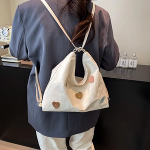 White leather hobo tote bag with colorful heart patches shown in a minimalist studio setting