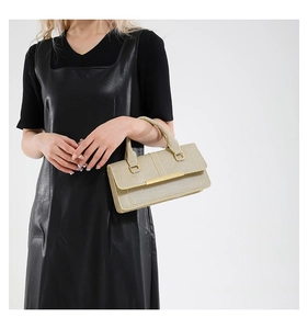 Femme en robe cuir noir tenant un sac à main tissé doré avec poignée métallique chic