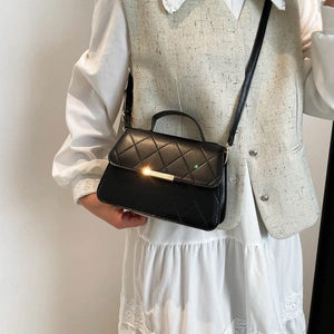 Sac bandoulière matelassé noir avec détails dorés porté par un mannequin en dentelle