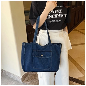 Detail der blauen Denim-Tragetasche mit Vordertasche und Goldknopf am Modell