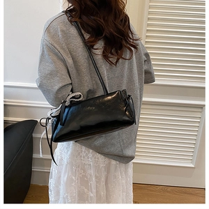 Detail view of glossy black underarm bag with delicate white lace and bow accents