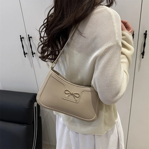 Minimalist beige shoulder bag with gold bow detail worn by model in a modern interior