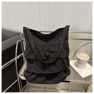Detail view of black canvas tote bag featuring three-layered ruffle pleats and long strap