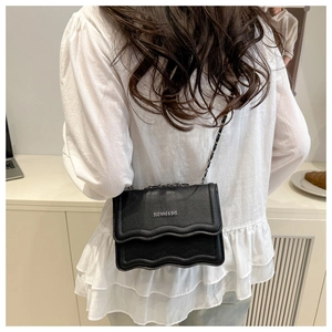 Detail view of black crossbody bag with lychee texture and wavy flap design on shoulder