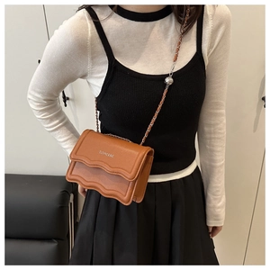 Close-up of brown leather crossbody bag with wave edge flap and silver chain strap