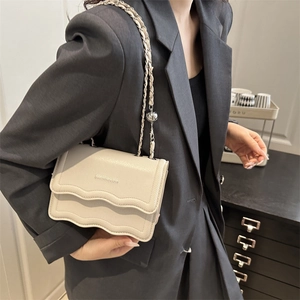 Beige faux leather crossbody bag with wavy flap and adjustable gold chain strap
