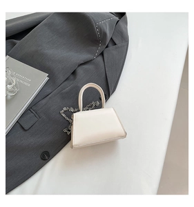 Mini cream leather crossbody bag with chain strap shown on a minimalist stylish tabletop