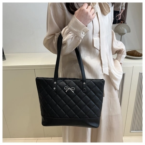 Detailed shot of quilted black tote bag with silver metal bow and shoulder straps