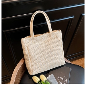 Detailed texture of hand-woven straw tote bag with cream leather handle on black chair