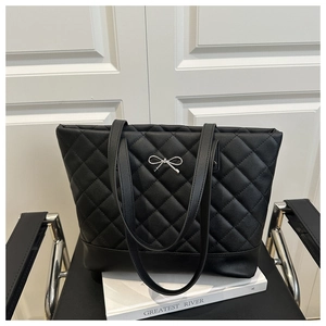 Detail of black quilted tote bag with silver bow accent and elegant faux leather texture