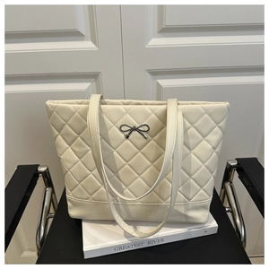 Detailed view of white quilted tote bag featuring a silver metal bow and rhombic pattern