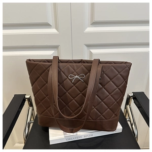 Macro detail of brown quilted PU leather tote bag with elegant silver metal bow charm