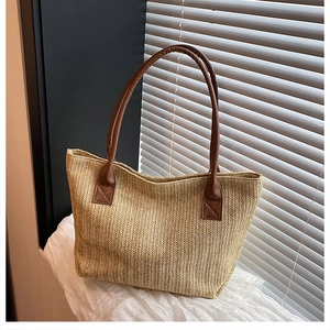 Detail of hand-woven straw tote bag with brown PU leather handles and reinforced stitching