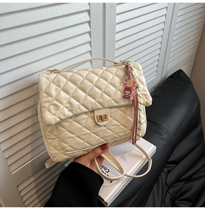 Detail einer beigen gesteppten Tasche mit goldenem Drehverschluss und Metallgriff