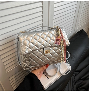 Detailansicht einer silbernen Stepptasche mit goldenem Drehverschluss und bunten Anhängern