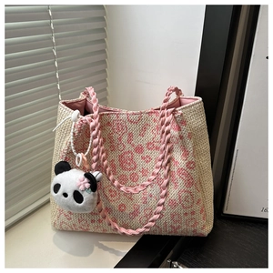 Detail of handwoven straw tote bag featuring pink heart patterns and panda charm