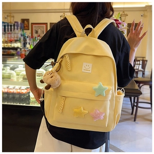 Detail of yellow canvas backpack with star plush patches and a brown bear charm