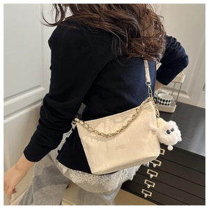 Détail d'un sac bandoulière blanc plissé avec chaîne dorée et pendentif en peluche