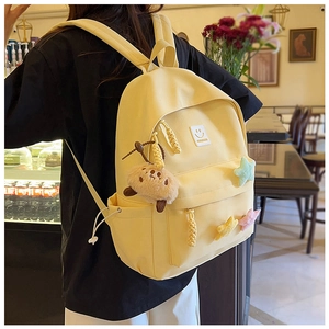 Detail of light yellow backpack with smiley patch, star studs and a plush bear pendant