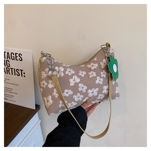 Close-up of beige fabric shoulder bag with white 3D floral crochet and a green charm