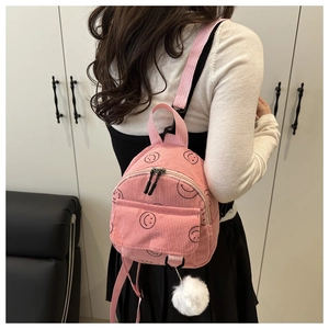 Close-up of pink corduroy mini backpack with cute smiley faces and plush ball charm