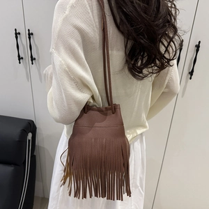 Sac seau marron à franges en cuir grainé porté par un mannequin en intérieur