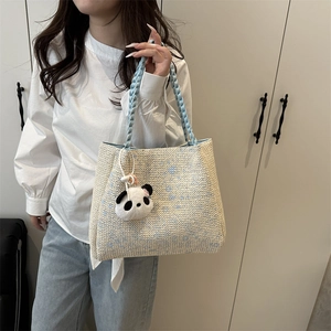 Large beige woven tote bag with blue handles and a panda charm shown with a model