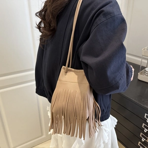 Sac seau minimaliste beige à franges avec bandoulière porté par un mannequin