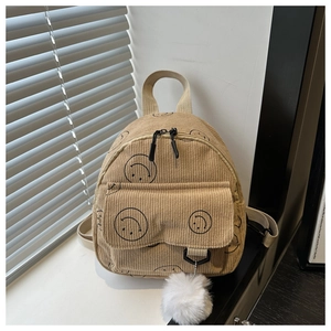 Detail of khaki corduroy backpack featuring smiley patterns and a white fur ball charm