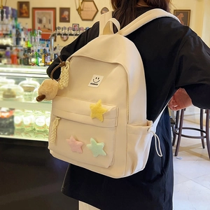 Beige canvas backpack with colorful plush stars and fuzzy ball pendant shown on model