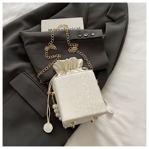 Macro detail of white snake-embossed mini bag with pearl charm and gold chain strap