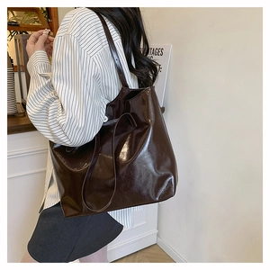 Detail view of large brown faux leather tote bag with glossy finish on model