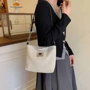Creamy corduroy tote bag with chain strap and teddy bear label in a cafe setting