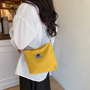 Yellow corduroy tote bag with pink leather chain strap and bear label on a female model