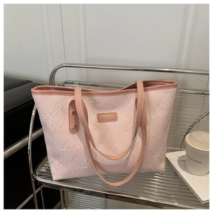 Detail of pink quilted tote bag showing intricate bow embroidery and gold metal logo plaque