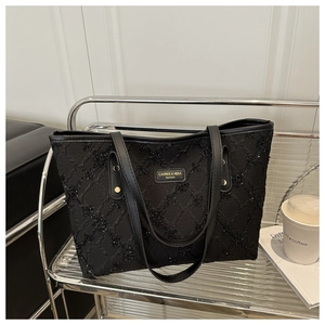 Detail of black pleated tote bag with golden logo plaque and metallic grid background