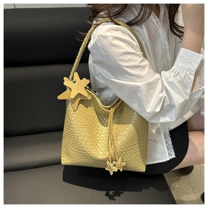 Gros plan détaillé d'un sac cabas tressé jaune avec breloques étoiles porté par un mannequin