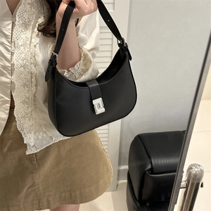 Minimalist black matte leather saddle bag with silver metal clasp held by a woman