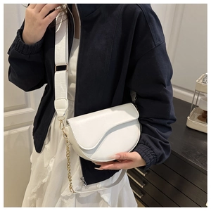 Detail view of white leather saddle bag with wide strap and decorative metal chain