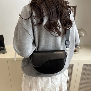 Retro black leather saddle bag with wide strap worn by model in a minimalist room