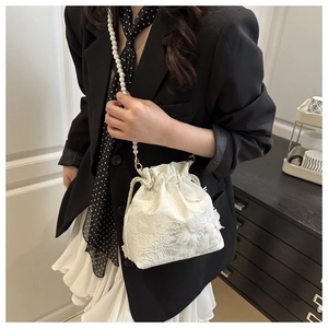 Detailed view of white lace drawstring bucket bag featuring a faux pearl crossbody strap