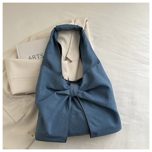 Détail du sac hobo en denim bleu avec un grand nœud et une texture tissée sur un blazer
