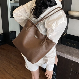 Deep brown litchi leather tote bag with silver buckle worn with a white casual outfit