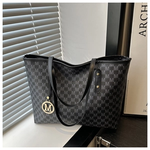 Close-up of grey monogram tote bag with black leather handles and gold metal M charm
