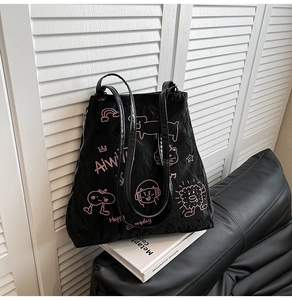 Detail of black tote bag with pink cartoon graffiti on a leather sofa with a book