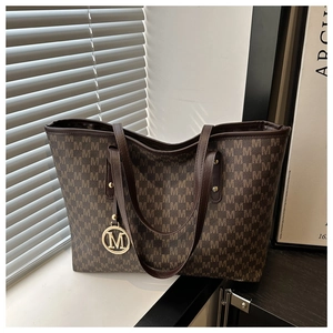 Detail shot of the large tote bag with retro brown M-pattern and gold logo charm