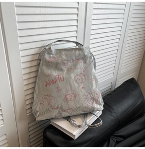 Detail of silver crinkled texture backpack featuring pink cartoon prints and metal luster
