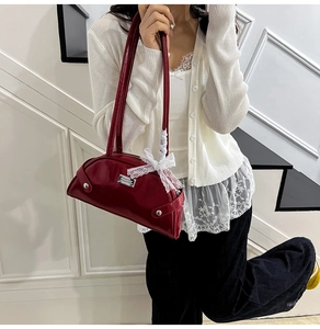 Detail of red patent leather shell bag with white lace bow and metallic stud accents