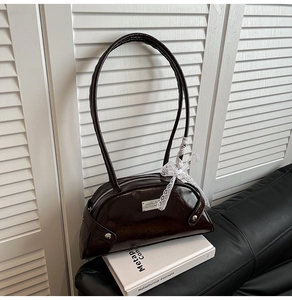 Detail of dark brown glossy patent leather bag with lace bow and silver logo plate